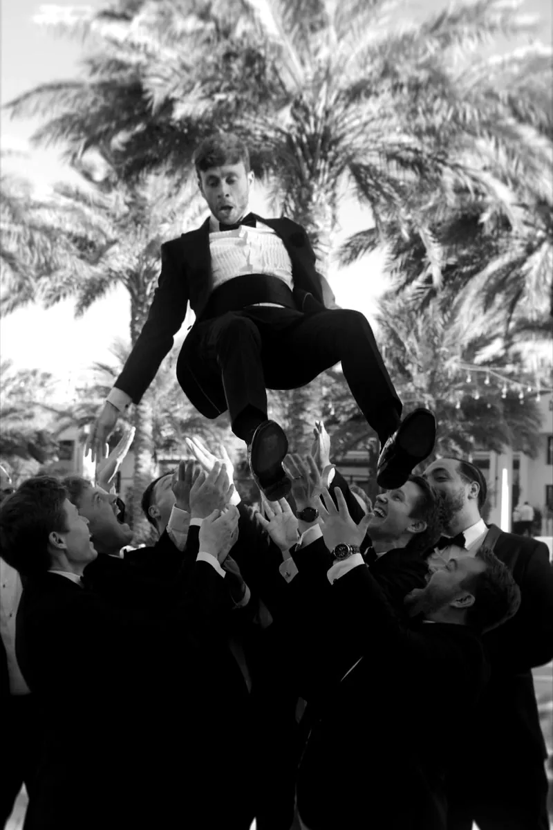 Groomsmen toss the groom into the air under palm trees
