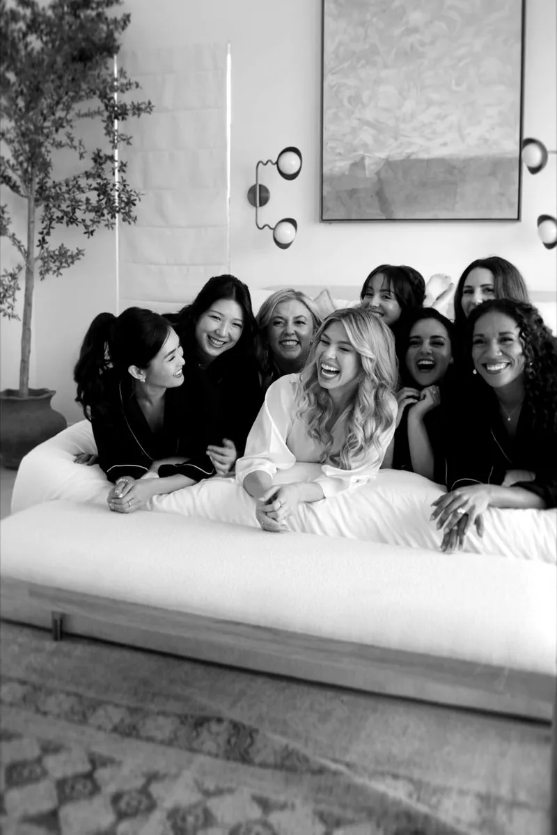 The bride laughing with her bridesmaids on a bed